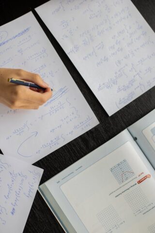 Close-up of a student answering questions with papers and textbook on a table.