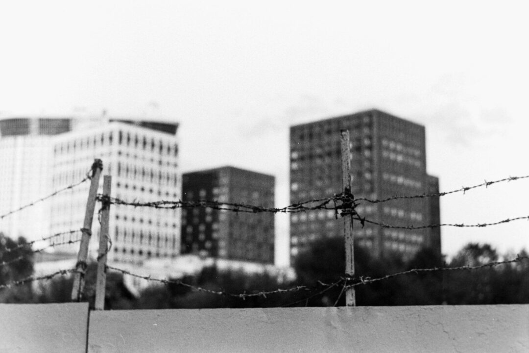 Barbed wire fence obstructs a view of buildings.