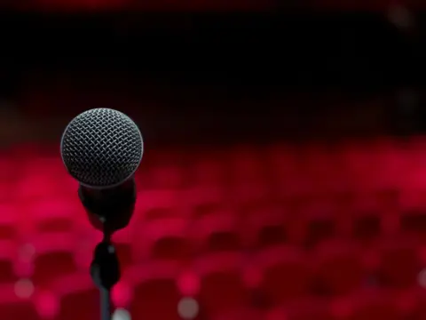 Comedy, Controversy And The Constitution: Free - Close-up of microphone on stage with empty red seats in background.