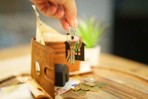 Hand holding keys with house charm and wallet. - Real Estate Transactions