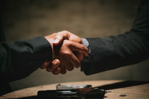 two people shaking hands over a wooden table - Agreement to Sell