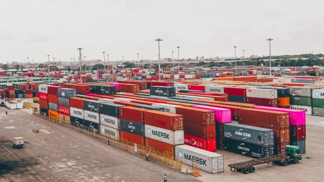 Press Note 3 (2026 Series): The - Colorful shipping containers stacked at a bustling port showcasing global trade.