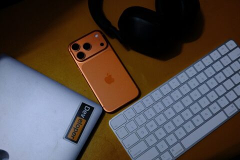Orange smartphone, laptop, keyboard, and headphones on desk.