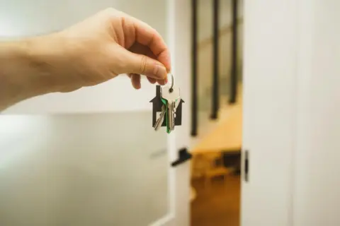 rera sale leasehold sub-lease - Sale - A hand holding a house key indoors signifies new ownership or leasing in real estate.