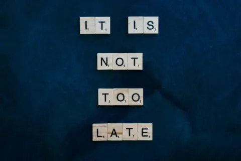 487 days - 487 Days Too - An inspiring message formed with wooden letter tiles on a dark surface: 'It is not too late'.