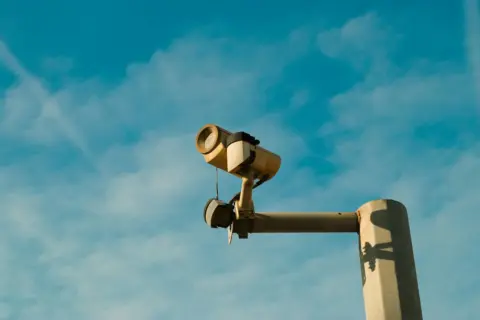 madras high court cctv surveillance privacy - A surveillance camera mounted outdoors against a bright blue sky, symbolizing s