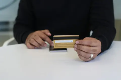 s.o. 2702(e) wage ceiling provident fund - Person holding a credit card and smartphone, indoor close-up view.