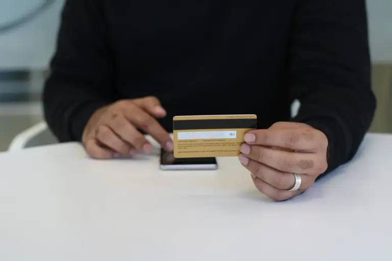 s.o. 2702(e) wage ceiling provident fund - Person holding a credit card and smartphone, indoor close-up view.