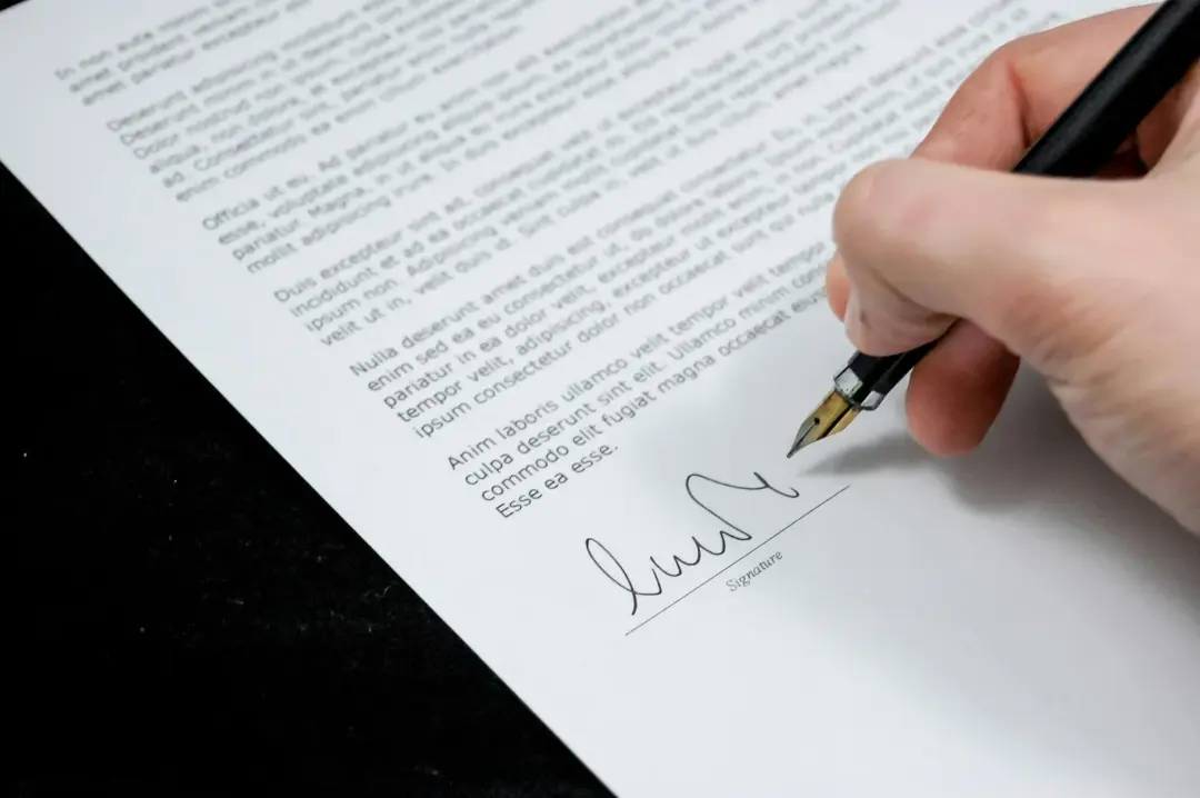 authorization letter curable defect secured asset - Close-up of a hand signing a formal document with a fountain pen, indicat