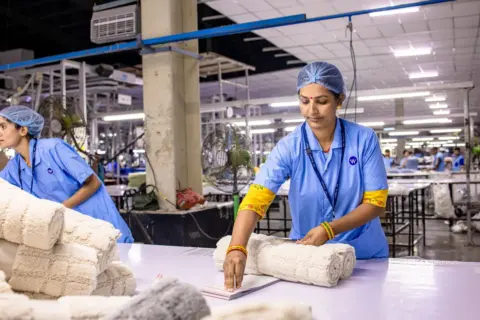 ecomark criteria environmental compliance product standards - Indian textile worker organizing fabric rolls in a factory sett