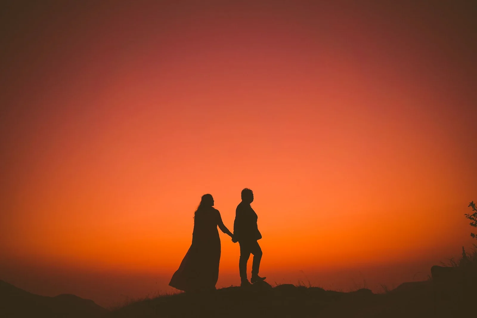 Silhouette of a couple holding hands against a vibrant sunset in Mandav, Madhya Pradesh.