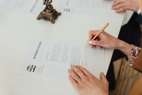maintenance decree death husband estate - - Close-up of hands signing a divorce decree document on a desk, showcasing legal p