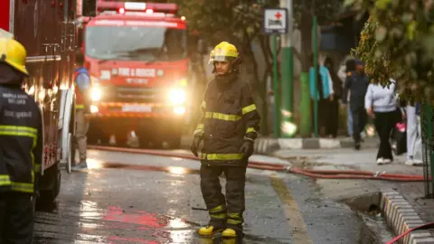 Third-Party Auditors, Digital Monitoring, and Administrative - Firefighter in uniform stands near a fire truck in the street