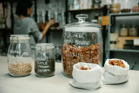 Towards Uniform Vegan Labelling in India: - Glass jars with organic chickpeas, pepper, and crispy banana on kitchen counter.