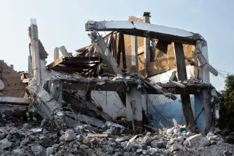 When the Wrecking Ball Waits: How - A partially demolished building showcasing exposed beams and rubble at an urban site.